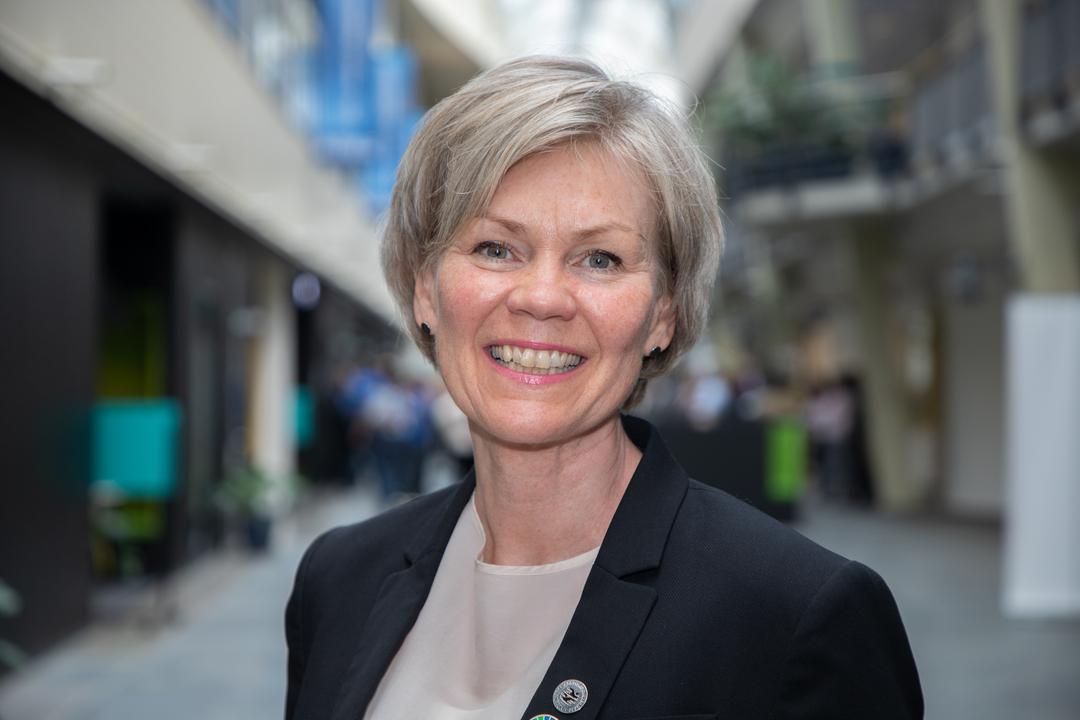 Lyshåret kvinne i dressjakke smiler til kamera